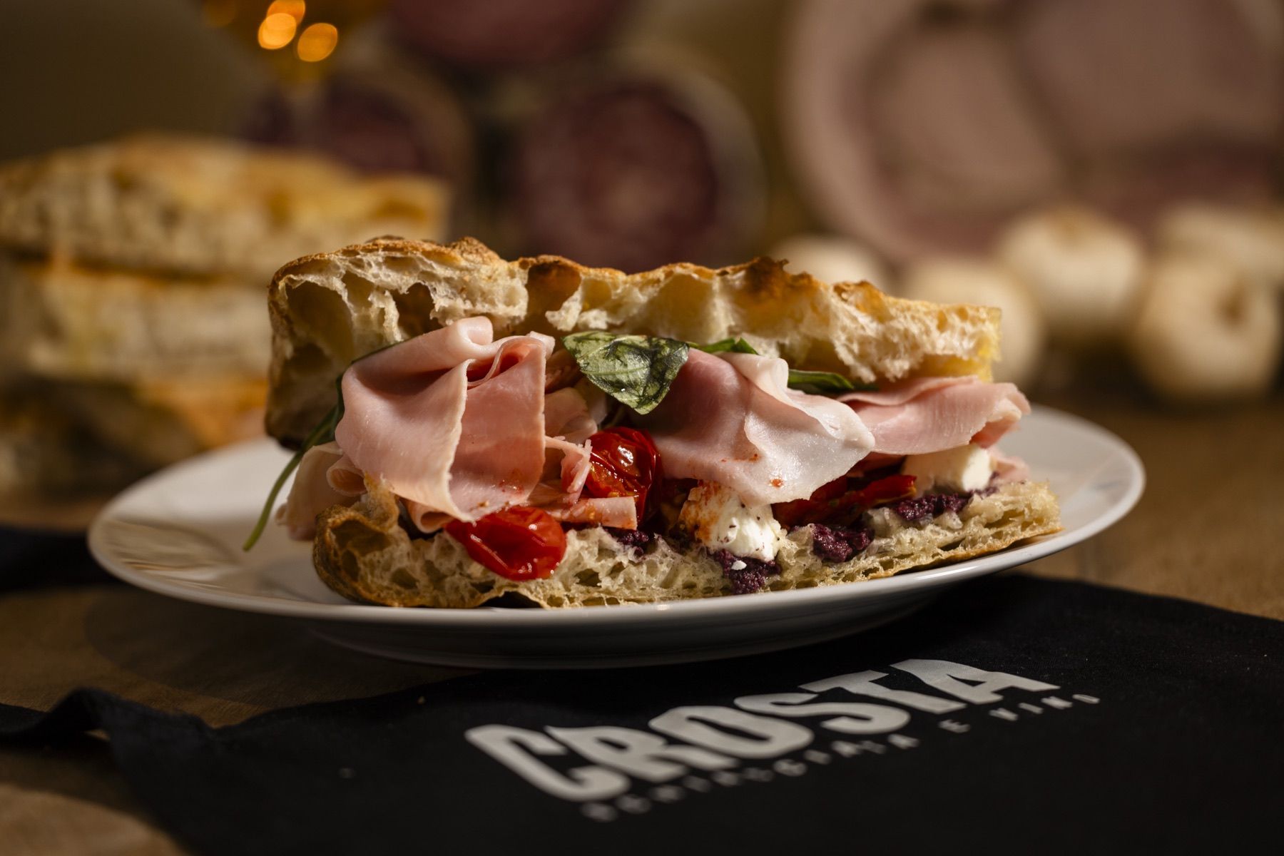 Mortadella schiacciata on a plate beside Italian cured meats