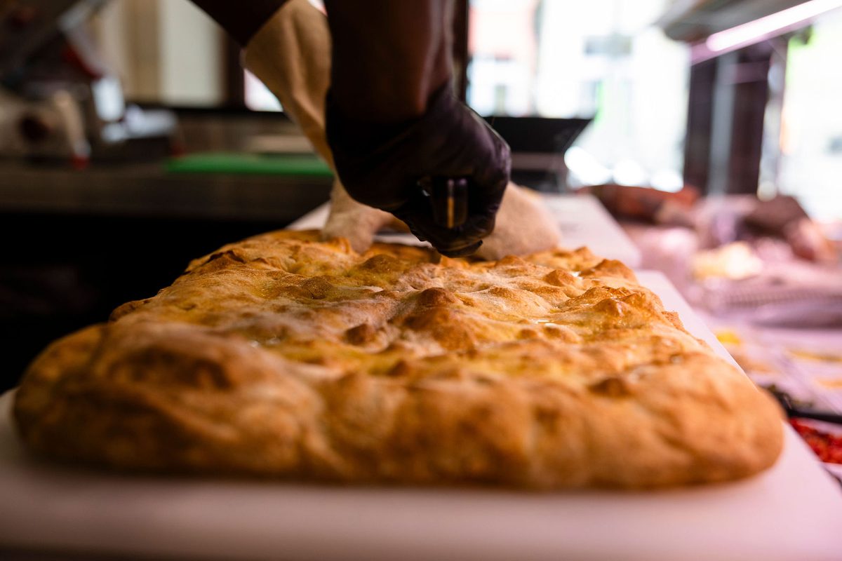A whole schiacciata fresh from the oven, golden and blistered, being finished on the counter