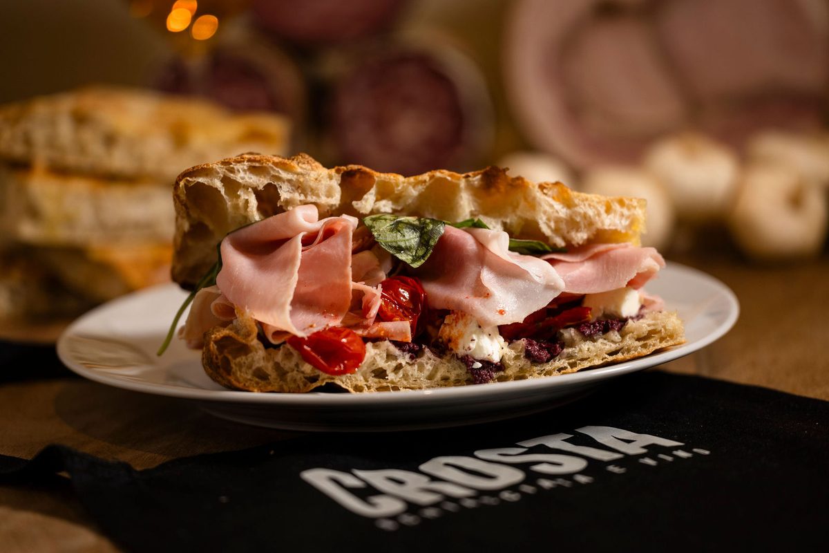 A schiacciata plated with mortadella, tomato confit, olive tapenade and basil
