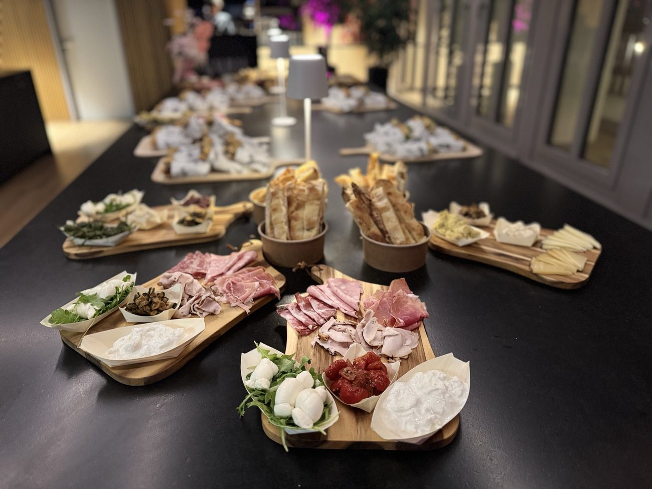 A long table of antipasti boards with mortadella, burrata, tomatoes and grissini