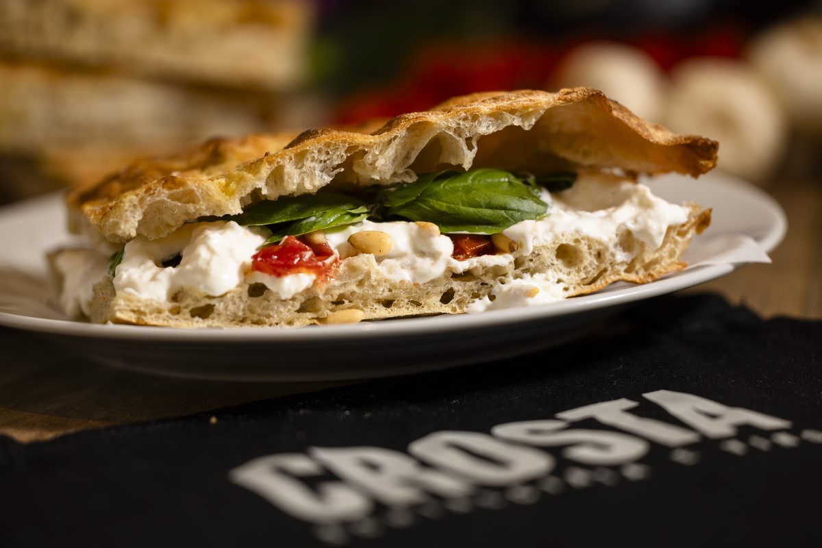 A schiacciata with stracciatella, tomato confit, pine nuts and basil on a plate