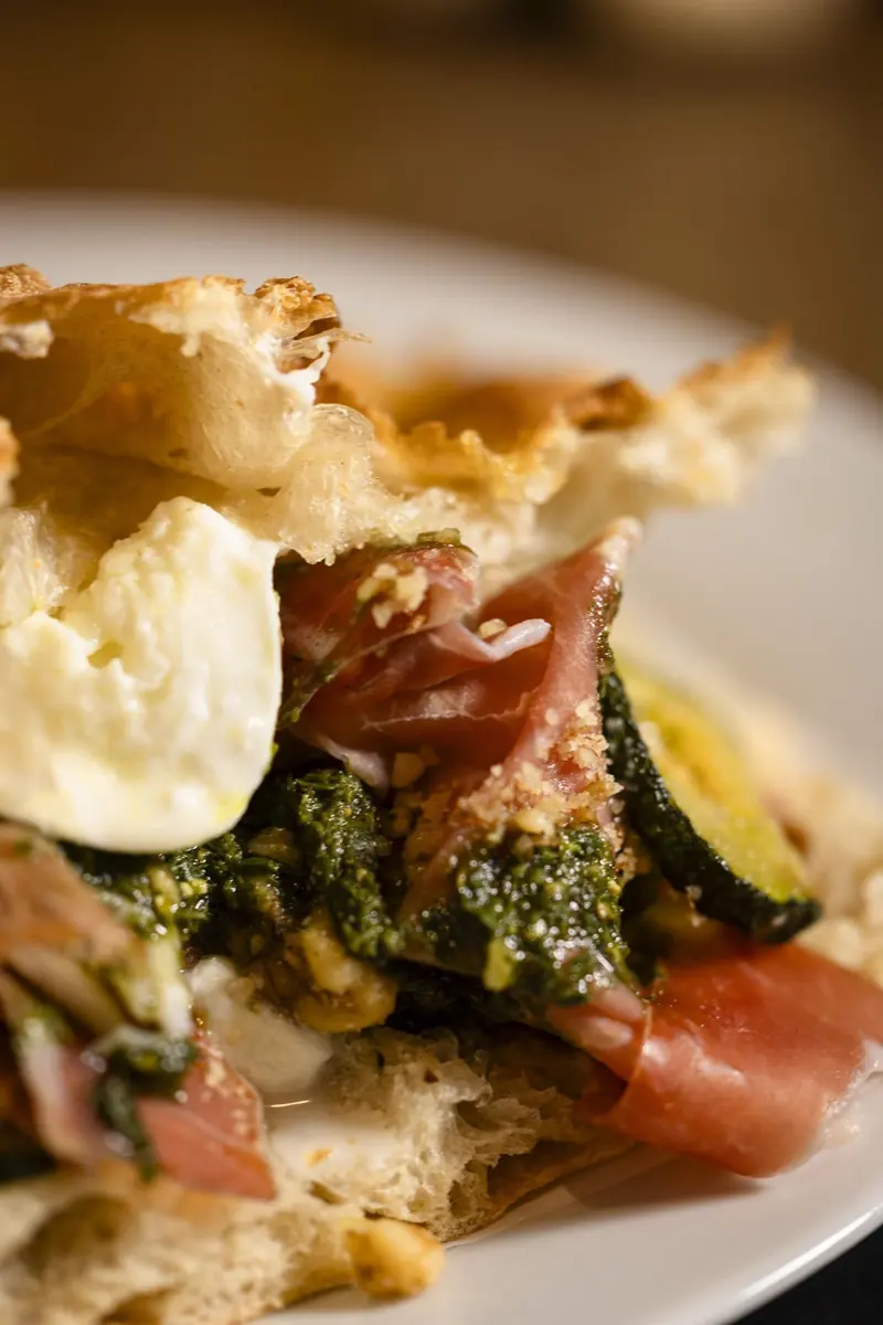 Schiacciata with prosciutto crudo, burrata and grilled courgette on a plate